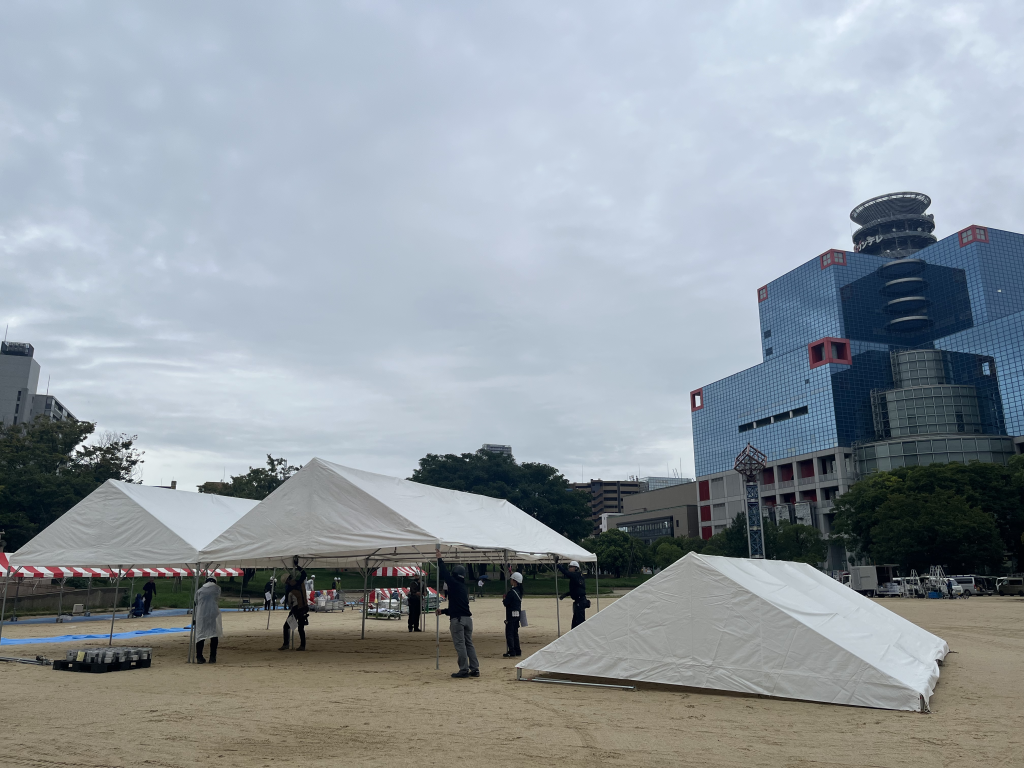 屋外イベント会場に設営されたテントと設営作業の様子